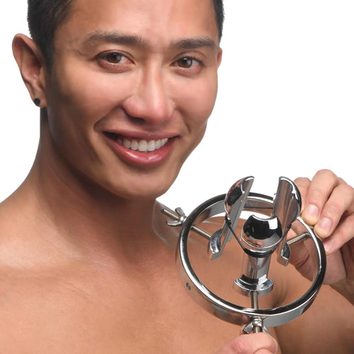 A smiling man holds a silver, stainless steel Master Series Forced Spread Anal Explorer with an adjustable ring design.