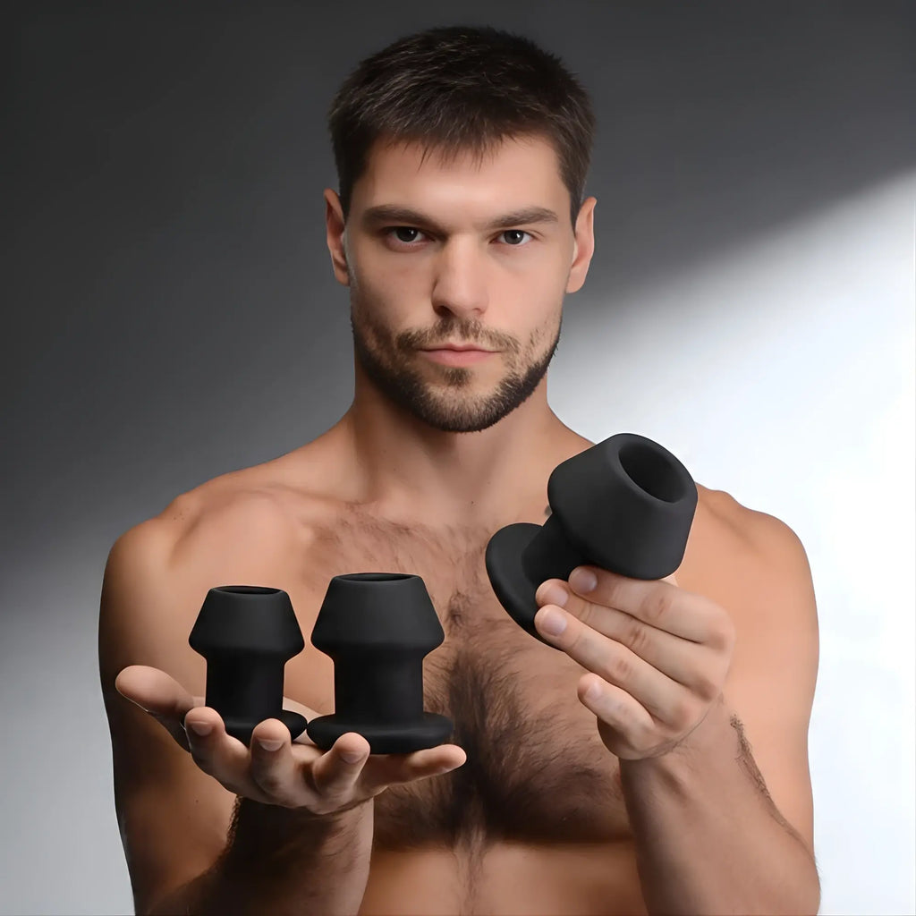 A man holding a Master Series Gape-Grommets 3-piece set of black, hollow silicone anal dilators of varying sizes.