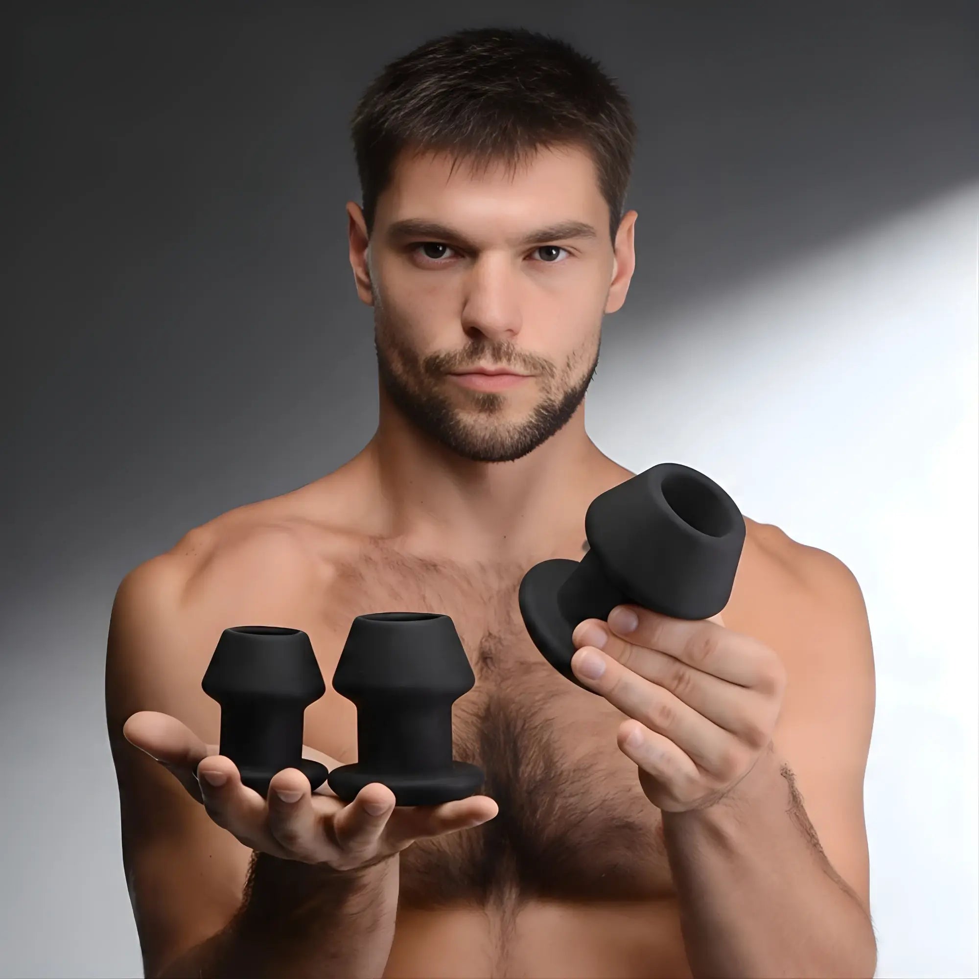 A man holding a Master Series Gape-Grommets 3-piece set of black, hollow silicone anal dilators of varying sizes.