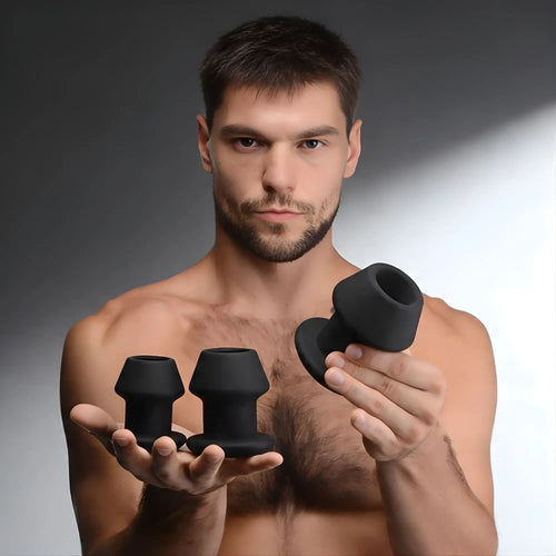 A man holding a Master Series Gape-Grommets 3-piece set of black, hollow silicone anal dilators of varying sizes.