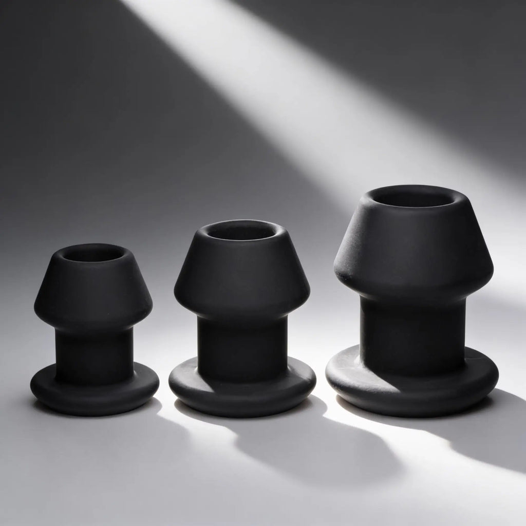 Master Series Gape-Grommets: A set of three graduated, matte black hollow silicone anal dilators on a grey background.