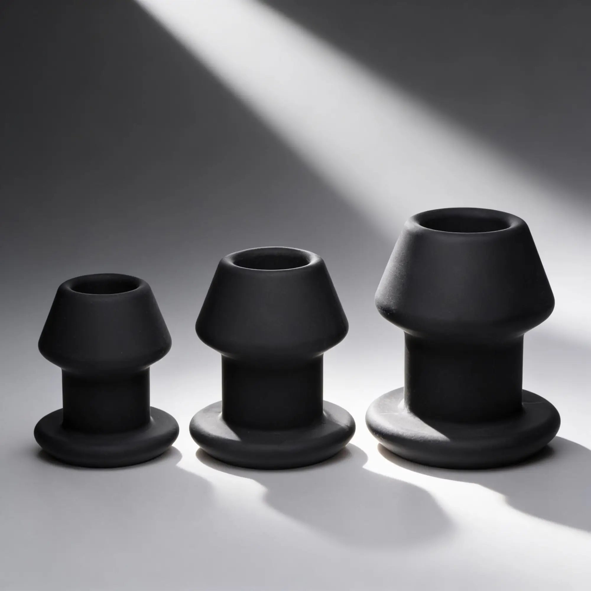 Master Series Gape-Grommets: A set of three graduated, matte black hollow silicone anal dilators on a grey background.