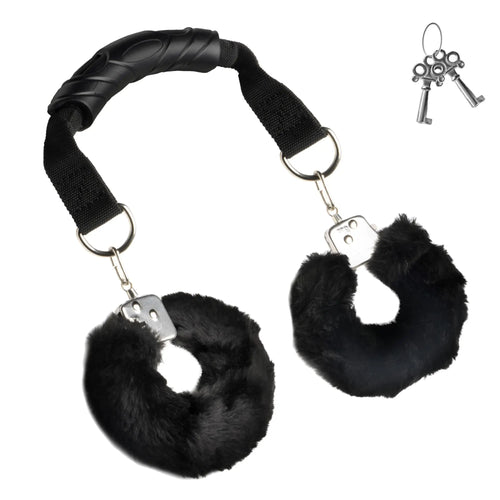 Master Series The Handler: black furry handcuffs attached by straps to a central black handle, with two keys.