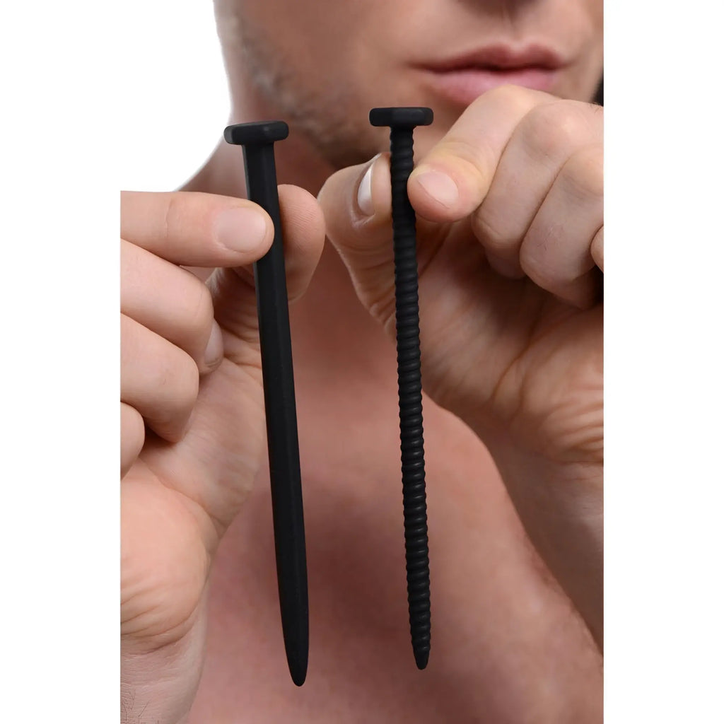 Hands hold two black, matte, nail-shaped silicone probes; one smooth, one with a spiral texture.
