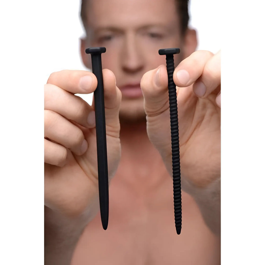 A man holds a smooth black silicone nail and a ridged black silicone screw from the Master Series Hardware collection.
