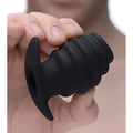 Hand holding a black Master Series Hive Ass Tunnel, a ribbed, hollow silicone anal plug with a flared base.