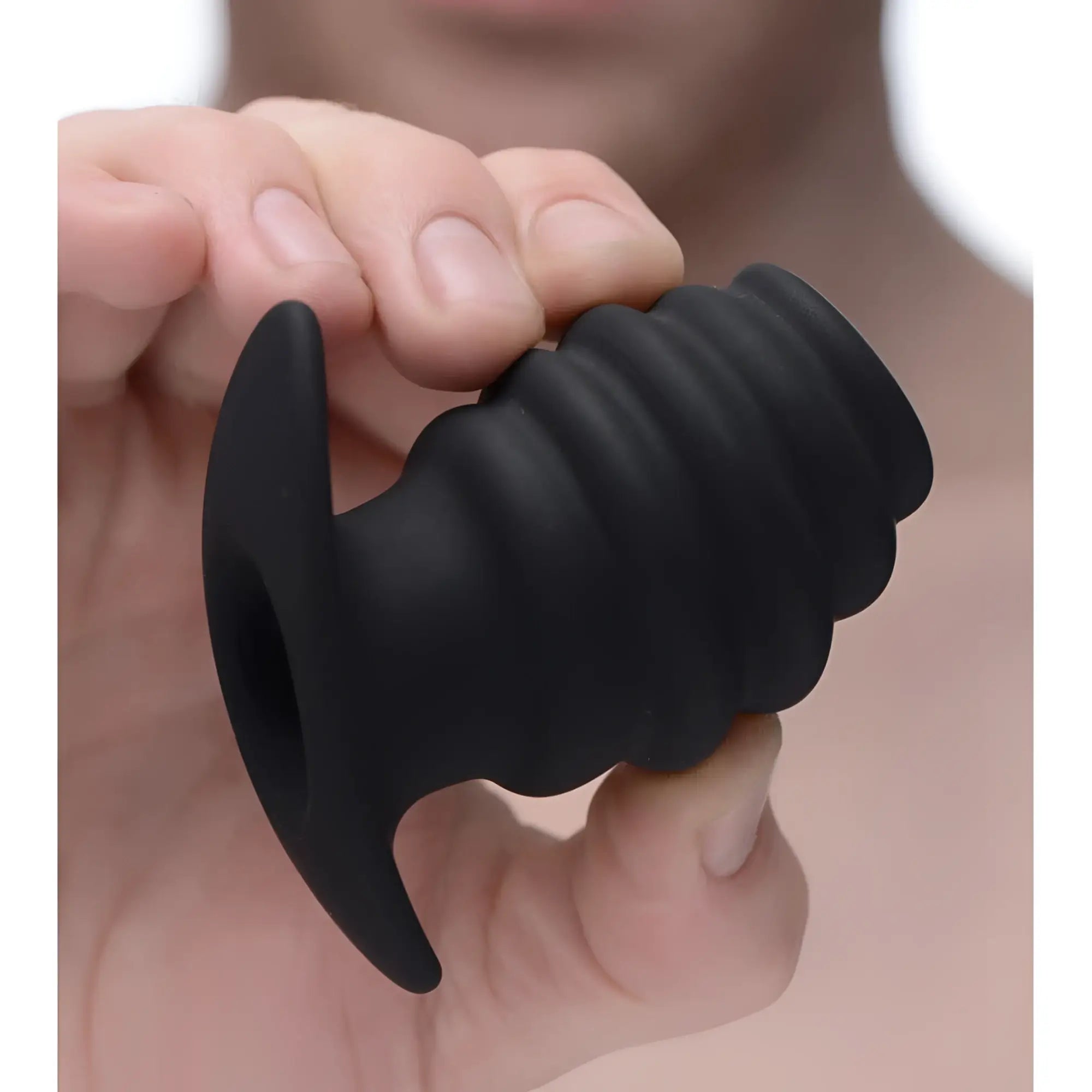 Hand holding a black Master Series Hive Ass Tunnel, a ribbed, hollow silicone anal plug with a flared base.