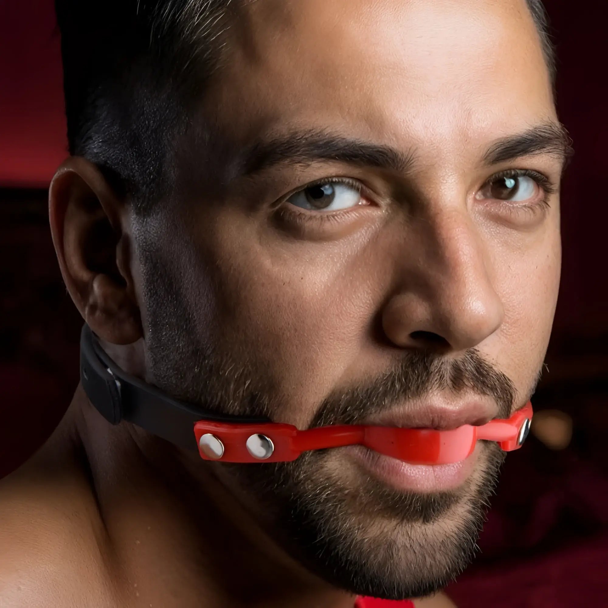 Man wearing a red Master Series Hush Comfort silicone ball gag with a black adjustable strap and silver hardware.