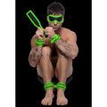 Master Series Kink in the Dark set: neon green cuffs, blindfold, and paddle worn by a tattooed man on black background.
