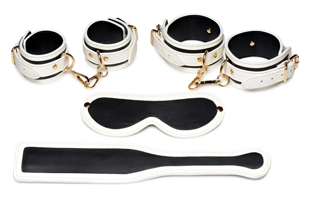 Master Series Kink in the Dark set: white and black leather cuffs, blindfold, and paddle with gold-tone hardware.