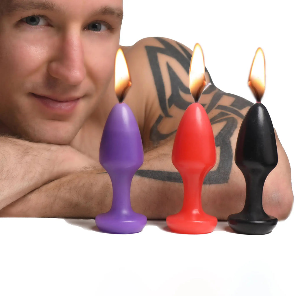 Master Series Kink Inferno Drip Candles: Three plug-shaped candles in purple, red, and black, all with lit flames.
