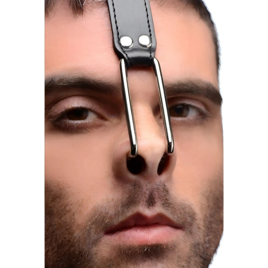 Close-up of a man wearing a black Master Series leather head harness featuring metal nose hooks.