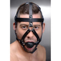 A man wearing a black Master Series leather head harness with silver hardware and a spherical ball gag.