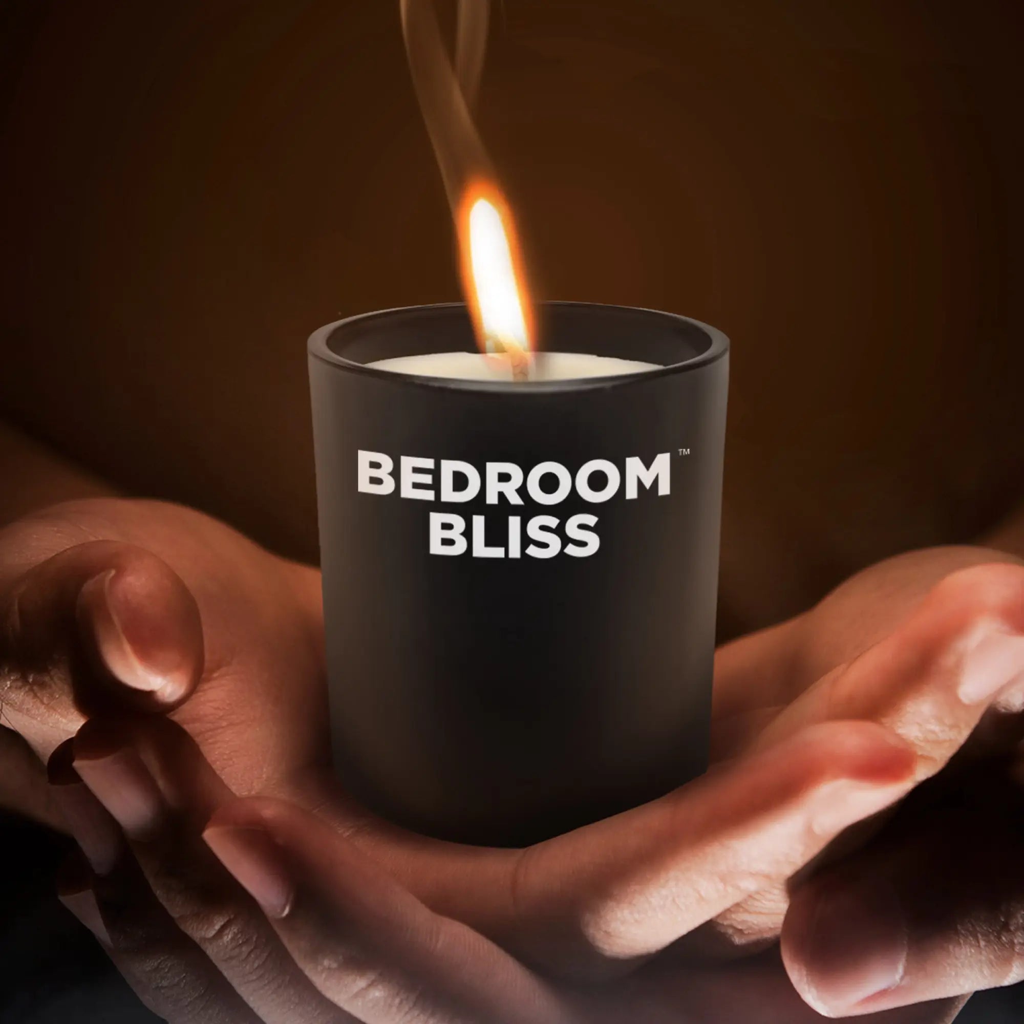Master Series Lover's Vanilla Massage Candle in a matte black jar, held in hands, with a lit wick and soft glow.