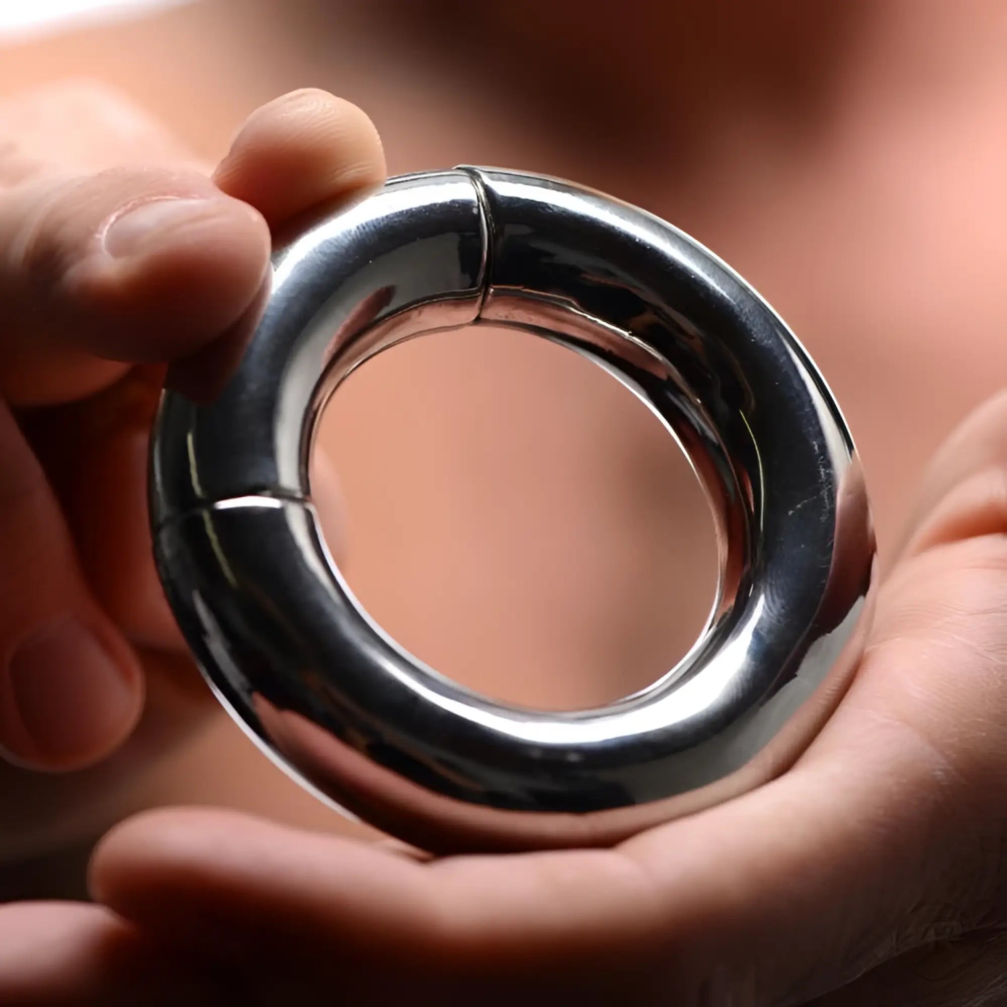 Hands holding a silver, circular Master Series Magnetize stainless steel magnetic ball stretcher.