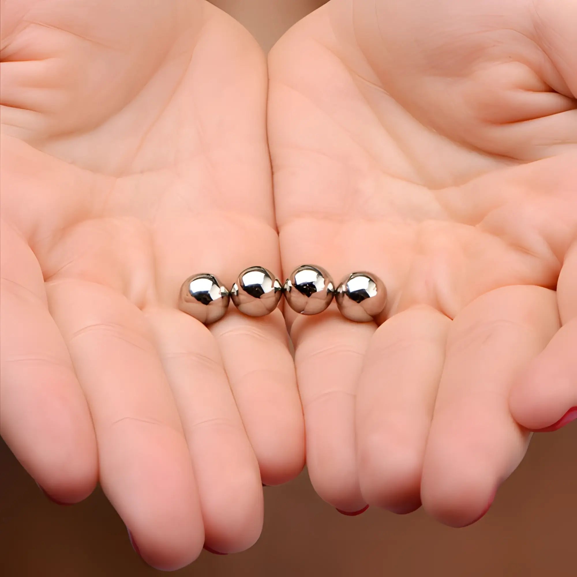Four shiny, metallic Master Series Magnus Mighty Magnetic Orbs held in a person's cupped hands.