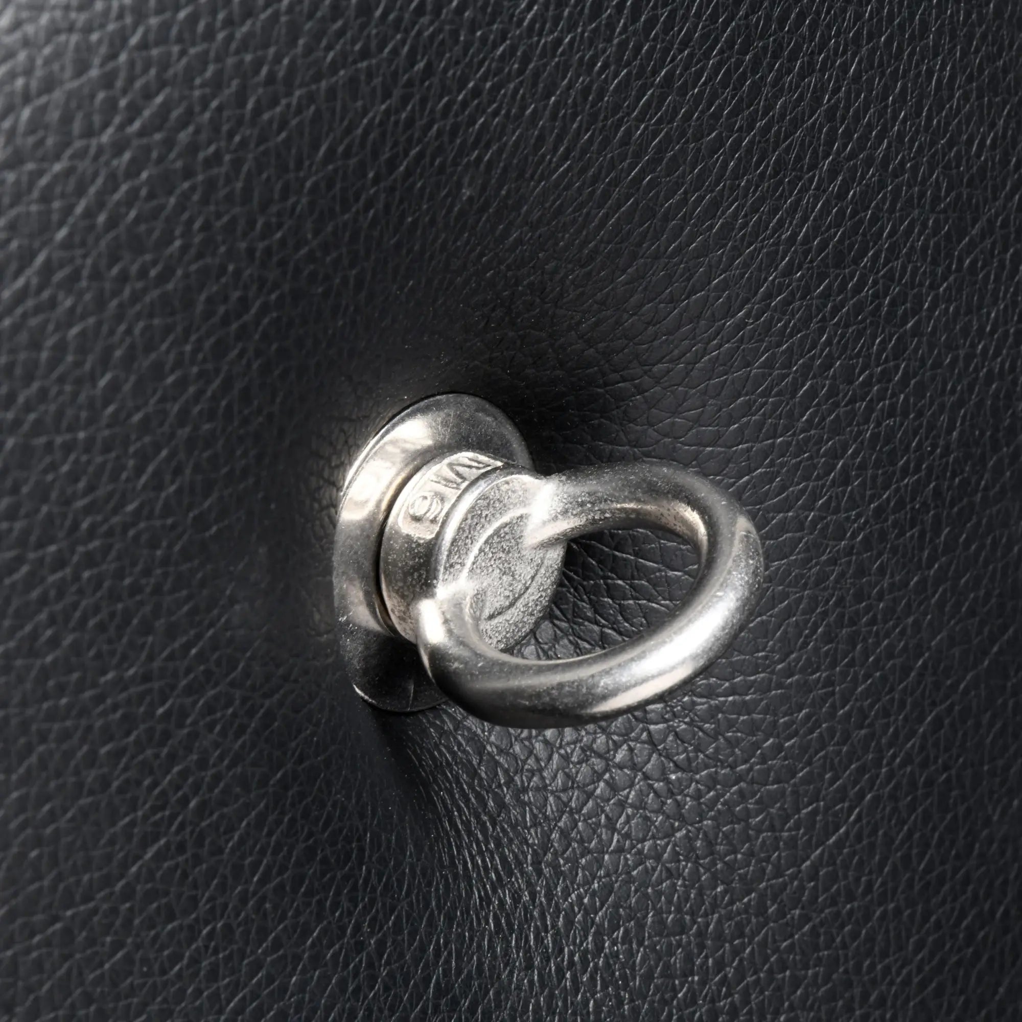 Close-up of a silver metal ring attachment on the textured black leather surface of a Master Series St. Andrew’s Cross.