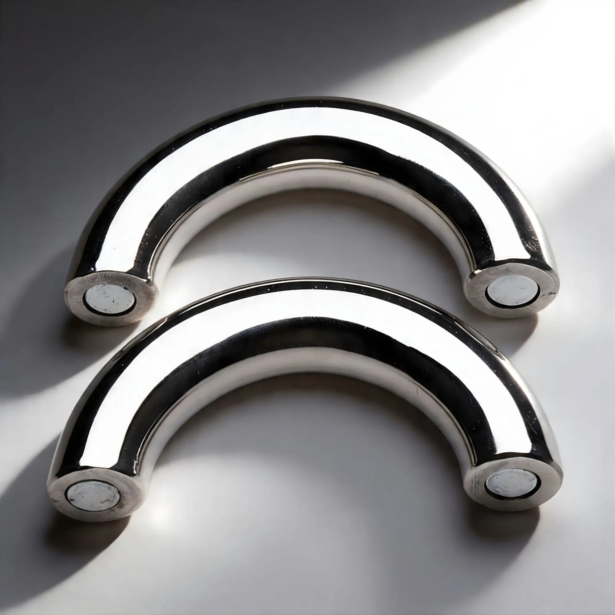 Two polished stainless steel Master Series Mega Magnetize curved magnetic cock rings on a white background.