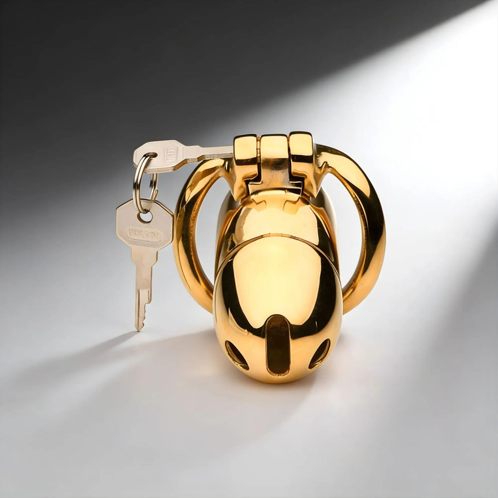 Master Series Midas 18K gold-plated locking chastity cage with a silver key, set against a studio background.