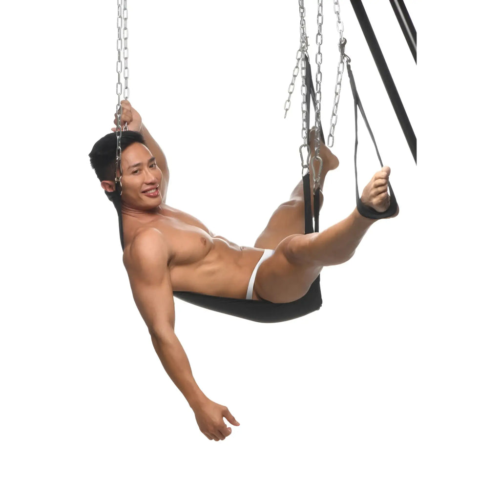 Master Series Nylon Sex Sling: A man sits in a black nylon sling suspended by metal chains against a white background.