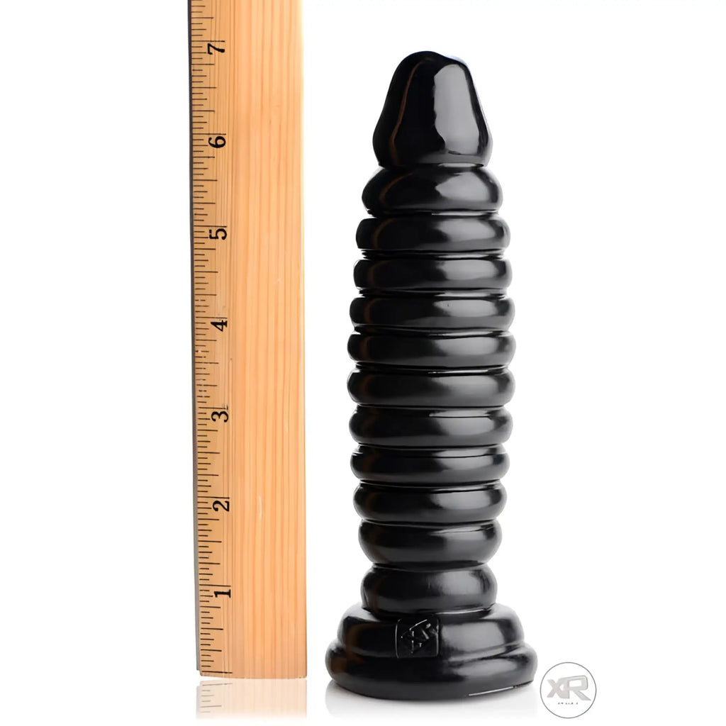 Master Series The Obsession 11 black, ribbed silicone butt plug beside a wooden ruler for scale against a white backdrop.