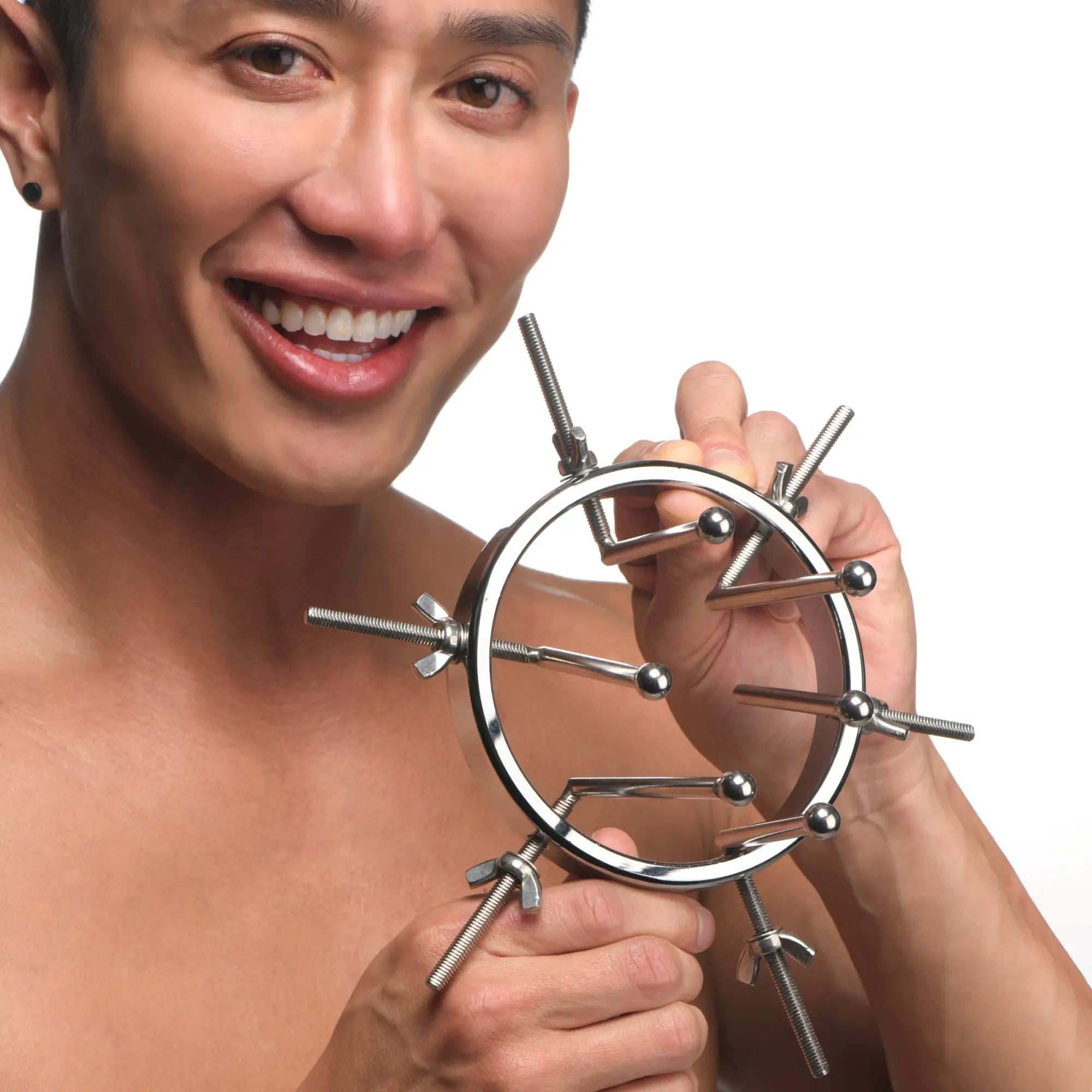 A smiling man holds a silver, circular Master Series Oculus Stainless Steel Anal Explorer with adjustable metal probes.