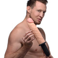 A man holding a tan, realistic Master Series Onslaught XXL vibrating thruster dildo with a black ribbed base.