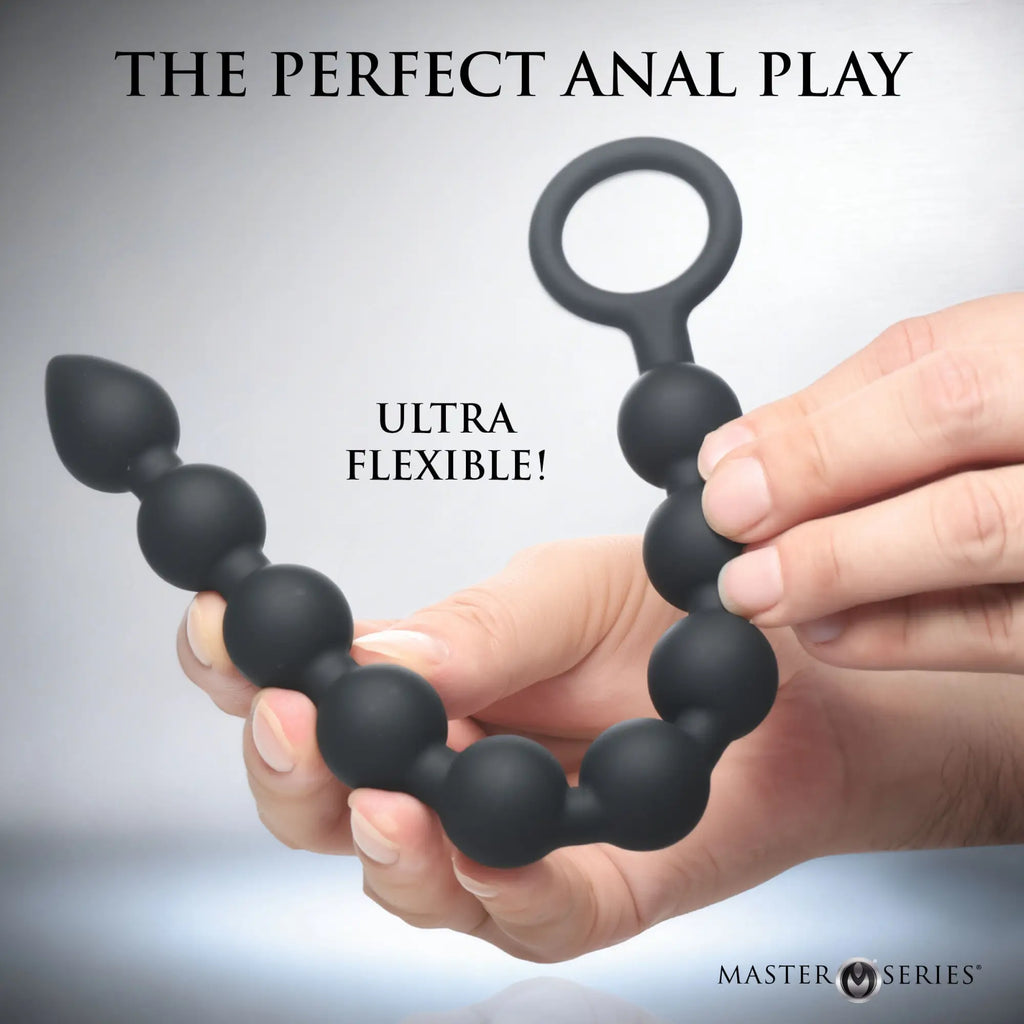 Master Series Pathicus: Flexible black silicone 9-bulb anal beads with a pull ring, held by a hand.