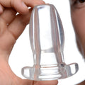 A hand holds a clear, hollow Master Series PeepHole anal plug against a white background.