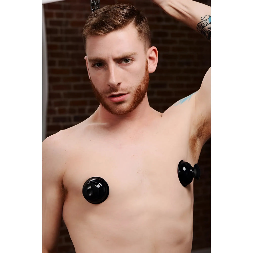 A man wearing black Master Series Plungers Extreme Suction silicone nipple suckers on his bare chest.