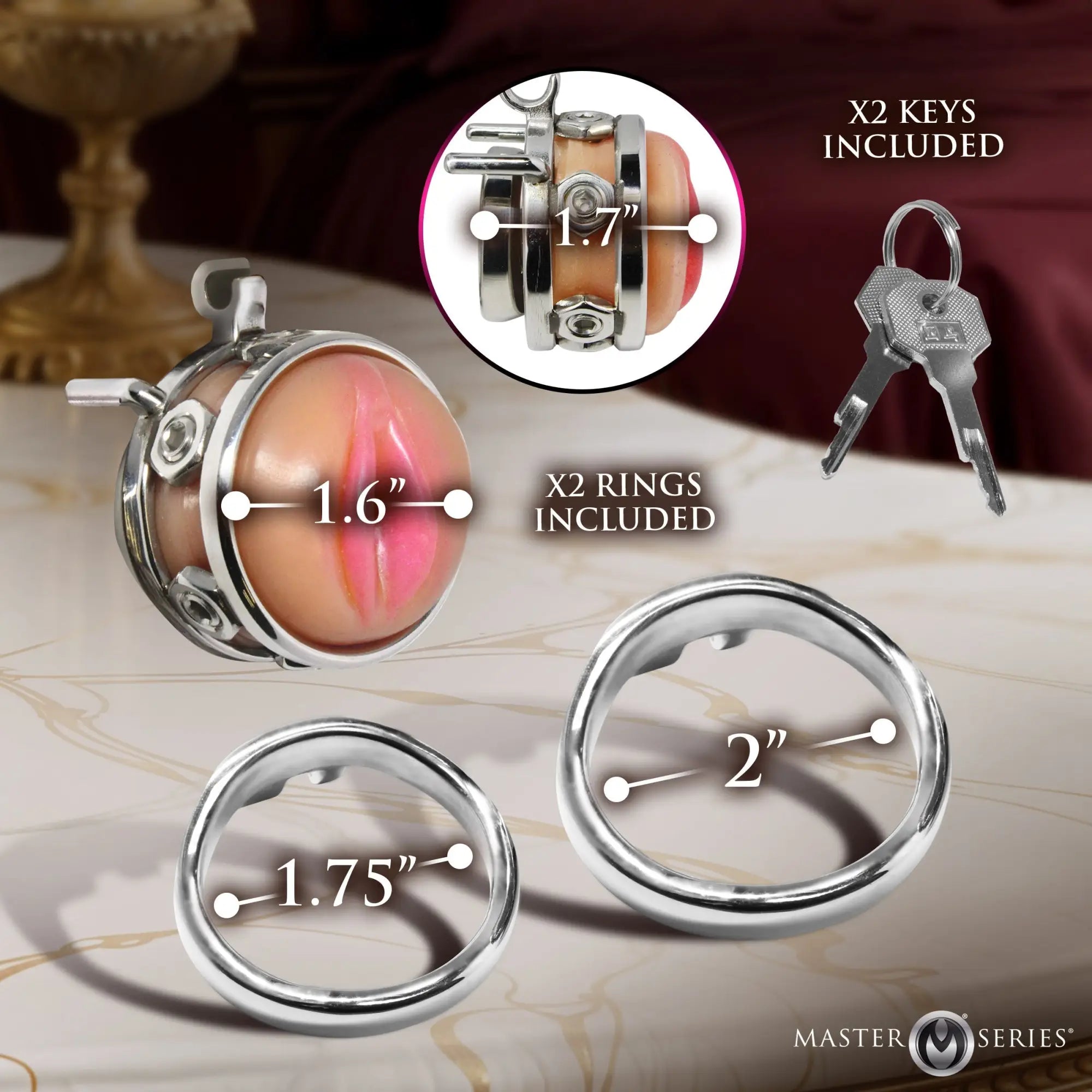 Master Series Pussy Boy metal chastity cage with two rings, two keys, and sizing dimensions labeled on a marble surface.