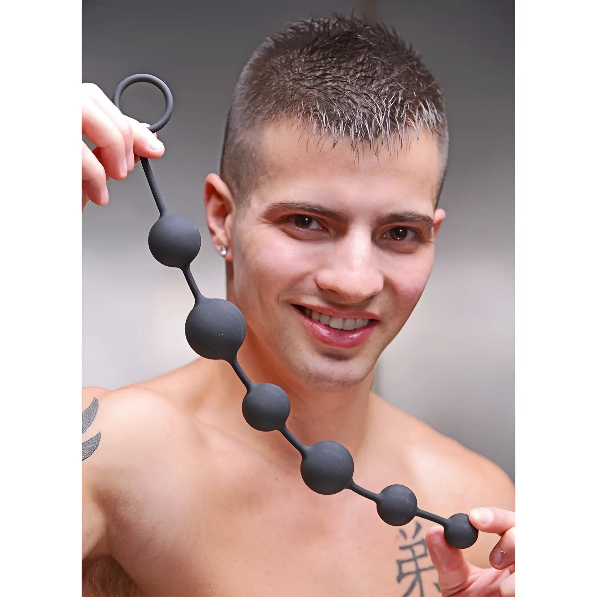 A smiling man holding a Master Series Serpent 6 black silicone anal bead toy with a pull ring in his hands.