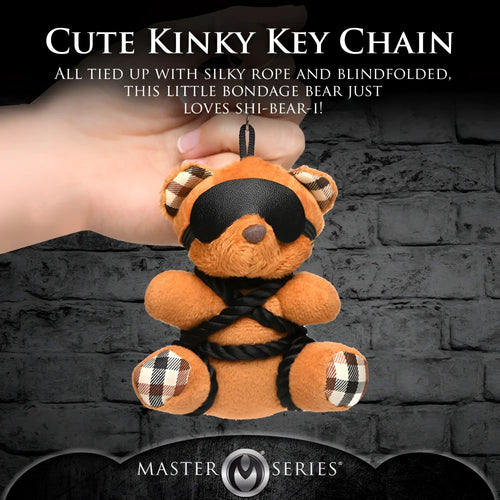 Master Series ShiBeari keychain: a tan teddy bear with a black blindfold and rope bondage details, held by a hand.