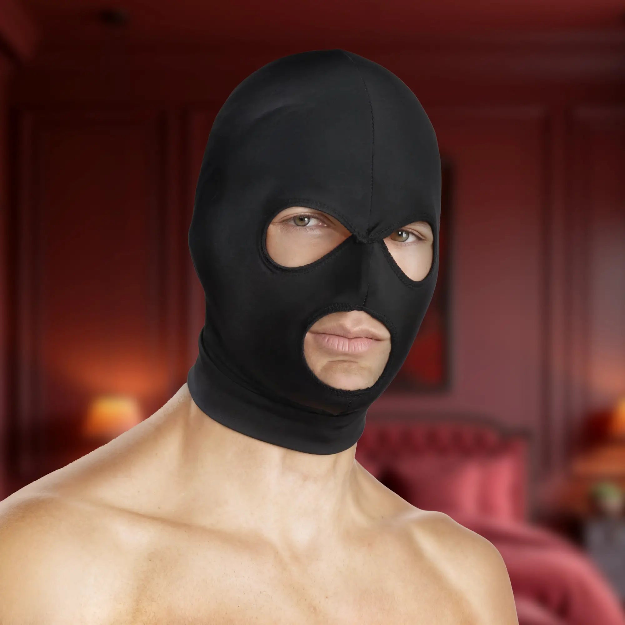 Black Master Series spandex hood with openings for eyes and mouth, worn by a shirtless man in a bedroom setting.