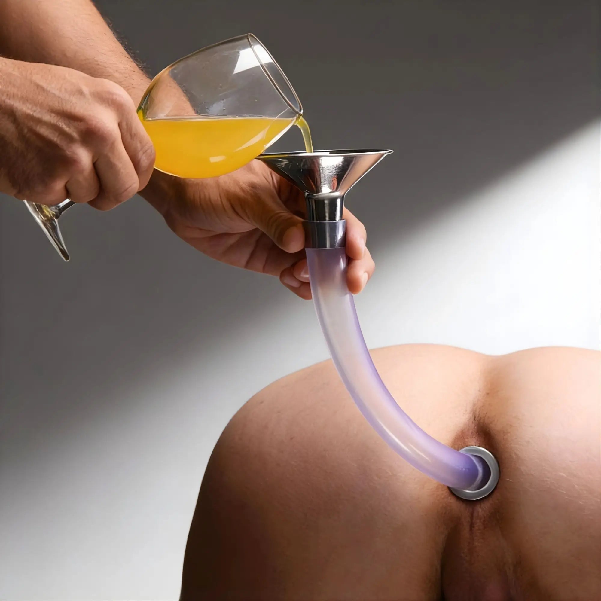Master Series stainless steel funnel with clear tubing connected to a hollow anal plug, with yellow liquid being poured in.