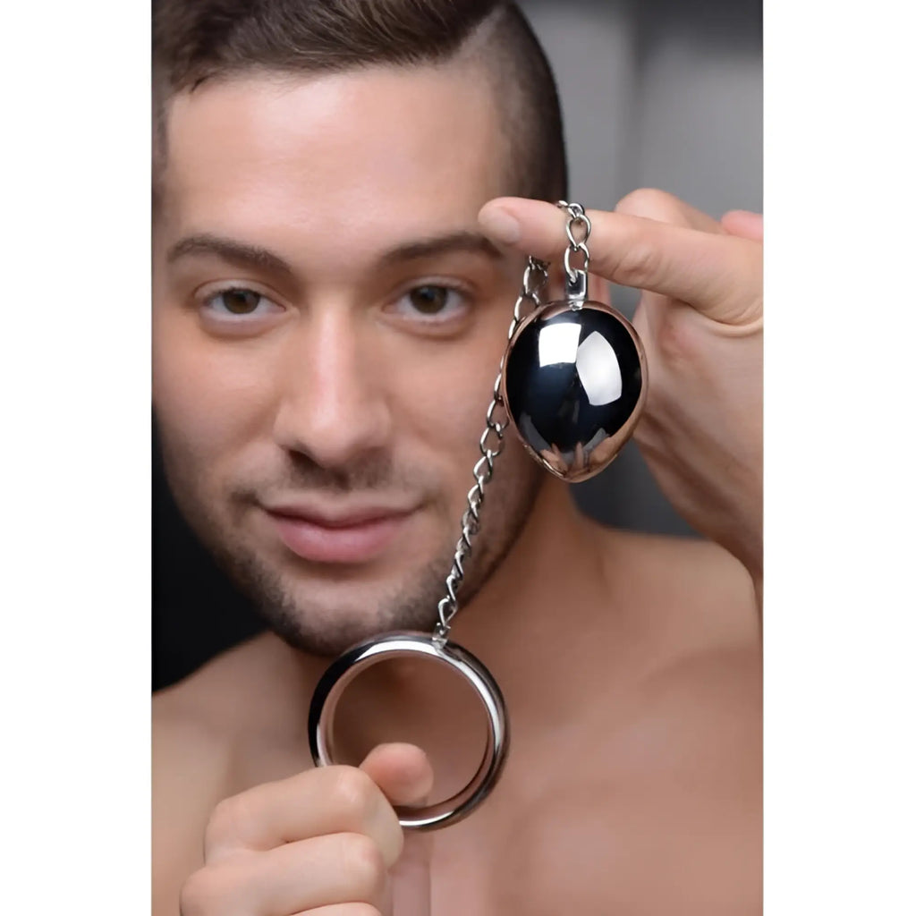 A man holds a Master Series stainless steel cock ring and anal plug connected by a metal chain.