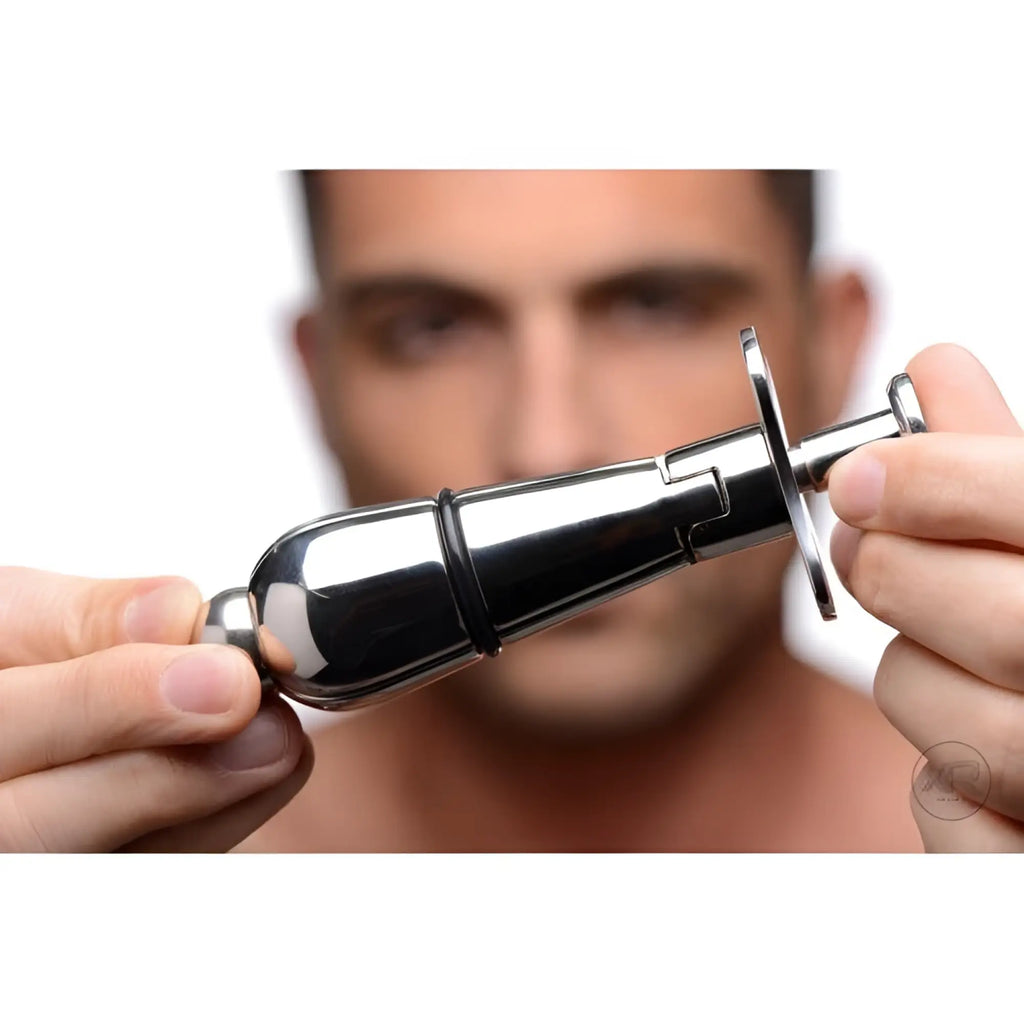 Hands holding a silver, tapered Master Series stainless steel locking anal plug against a blurred face.