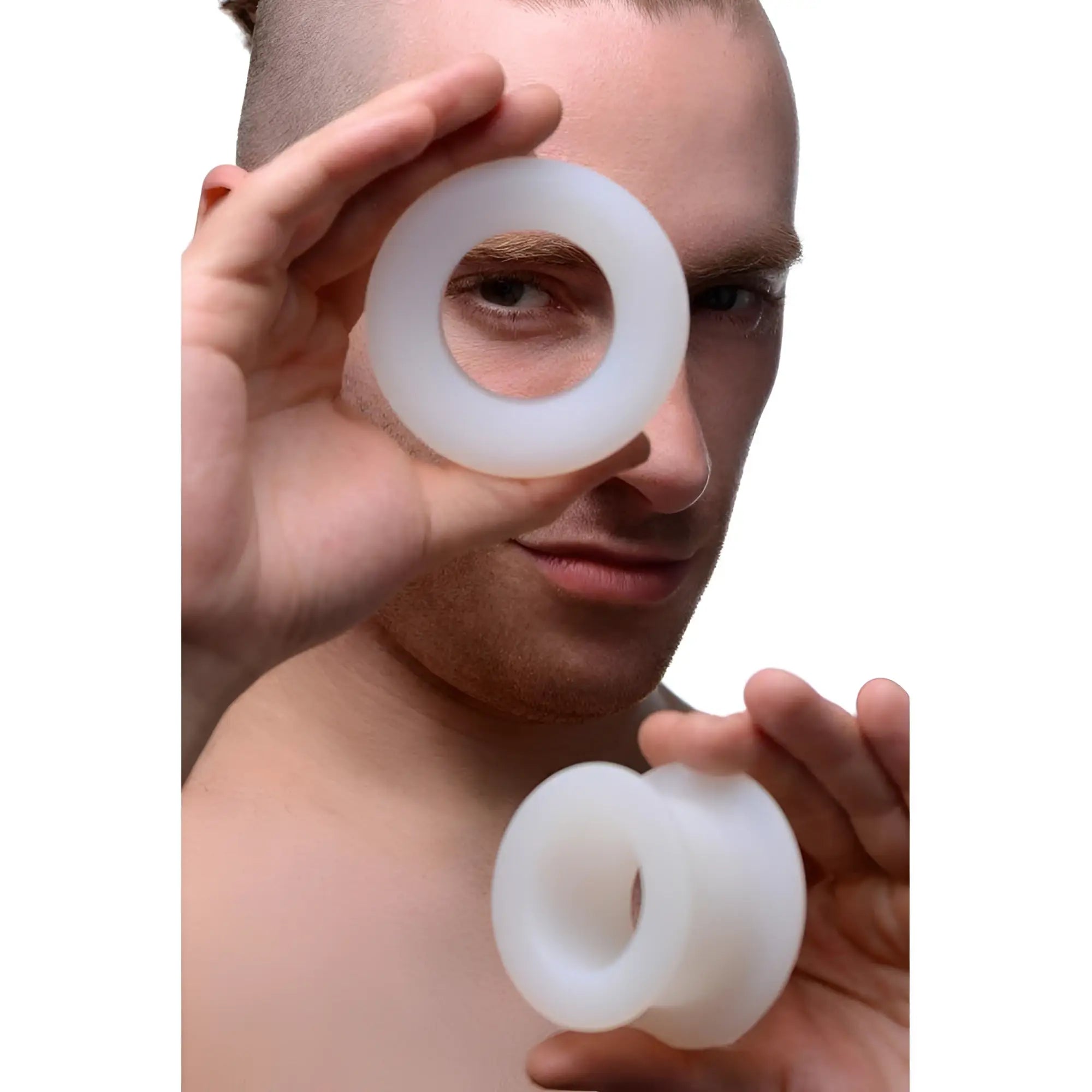 A person holds two smooth, white Master Series Stretch Master silicone grommets, one in front of each eye.