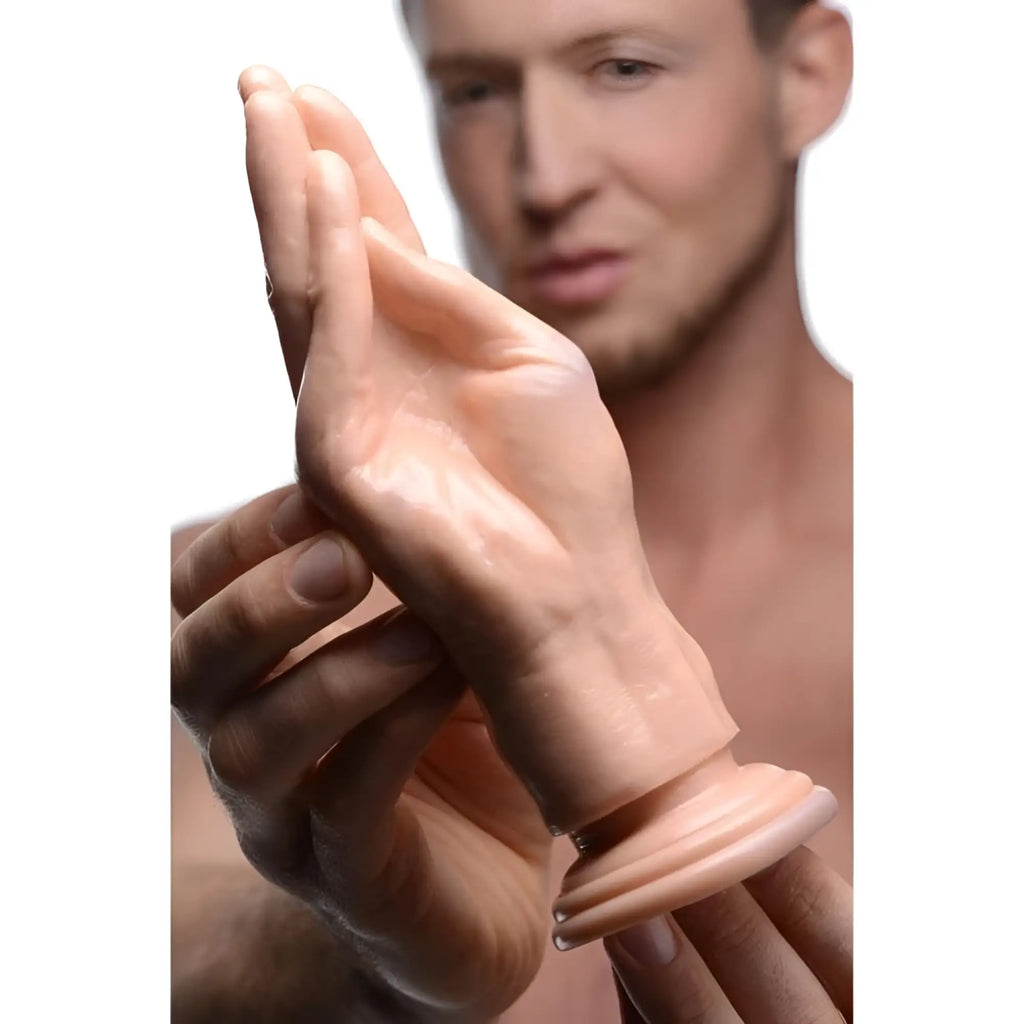 Master Series The Stuffer: A realistic, skin-toned silicone fisting hand dildo with a flared base, held by a man.
