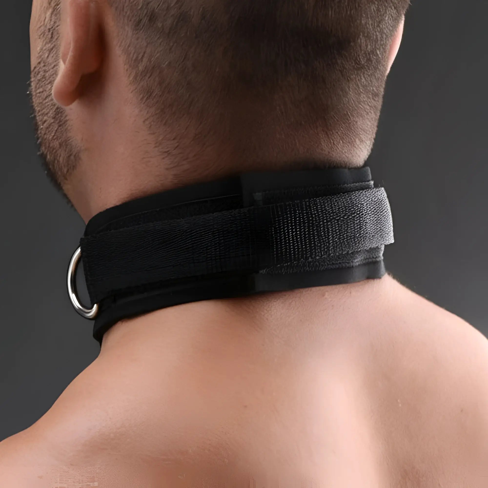 A person wears a black Master Series Submission collar with a silver O-ring on their neck against a gray background.