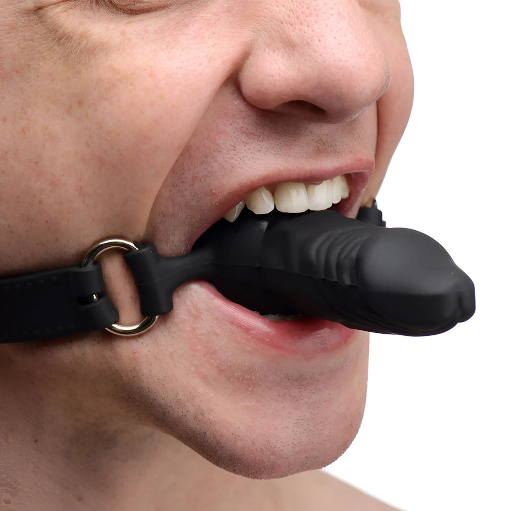 Master Series Suppressor black silicone phallic gag held in a person's mouth with a metal O-ring and adjustable strap.