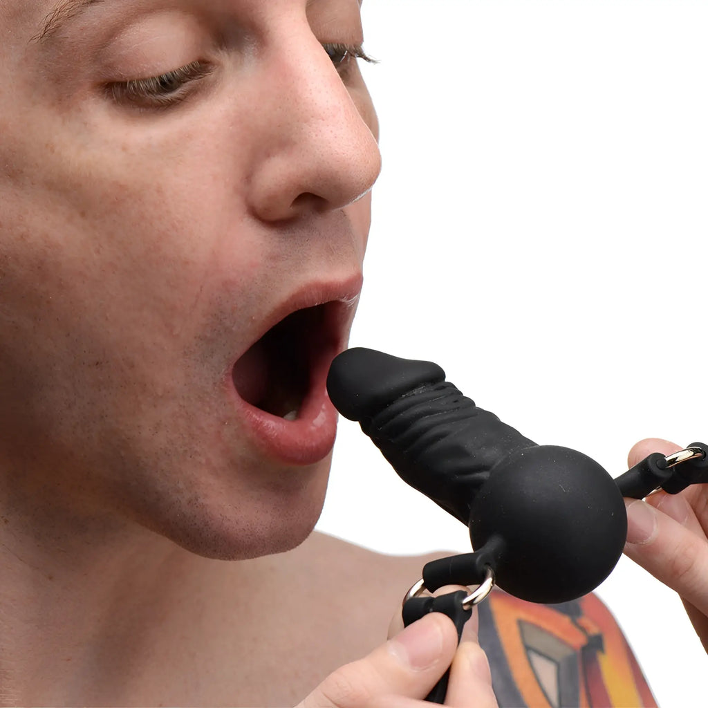 Master Series Suppressor Silicone Face Banger Gag featuring a black phallic-shaped silicone plug held near an open mouth.