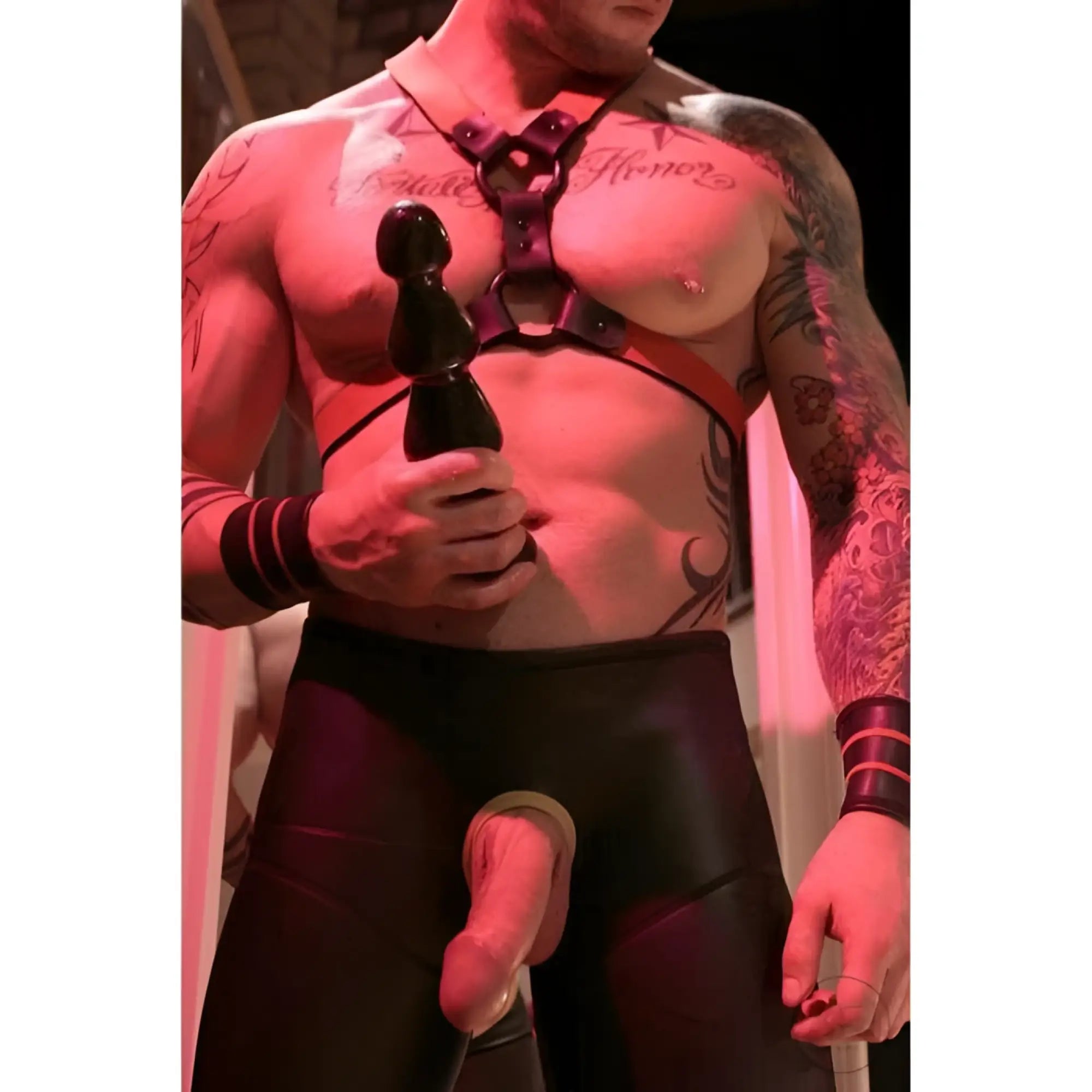 A man in a leather harness holds a black, multi-bump Master Series Three Bumps for Your Rump anal plug.