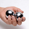 A hand holding two shiny Master Series Titanica Steel Balls against a plain white background.