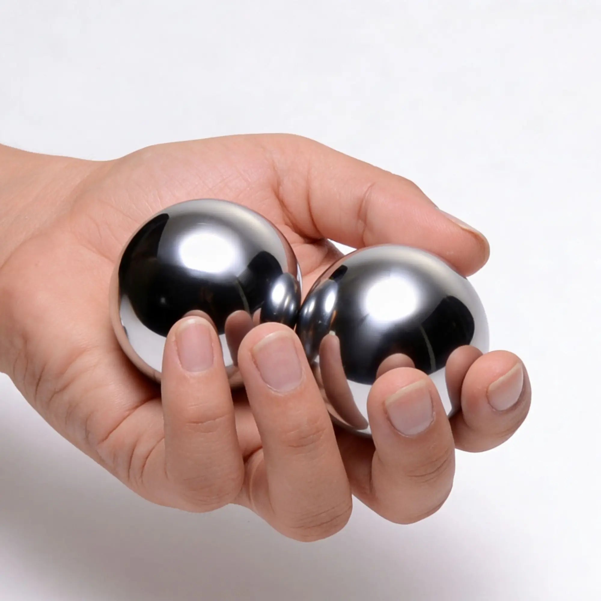 A hand holding two shiny Master Series Titanica Steel Balls against a plain white background.