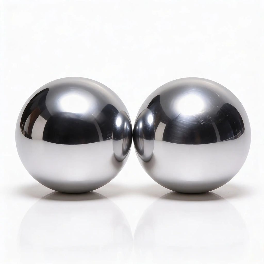 Two Master Series Titanica Steel Balls rest side by side on a glossy white surface, displaying mirrored reflections and striking highlights.