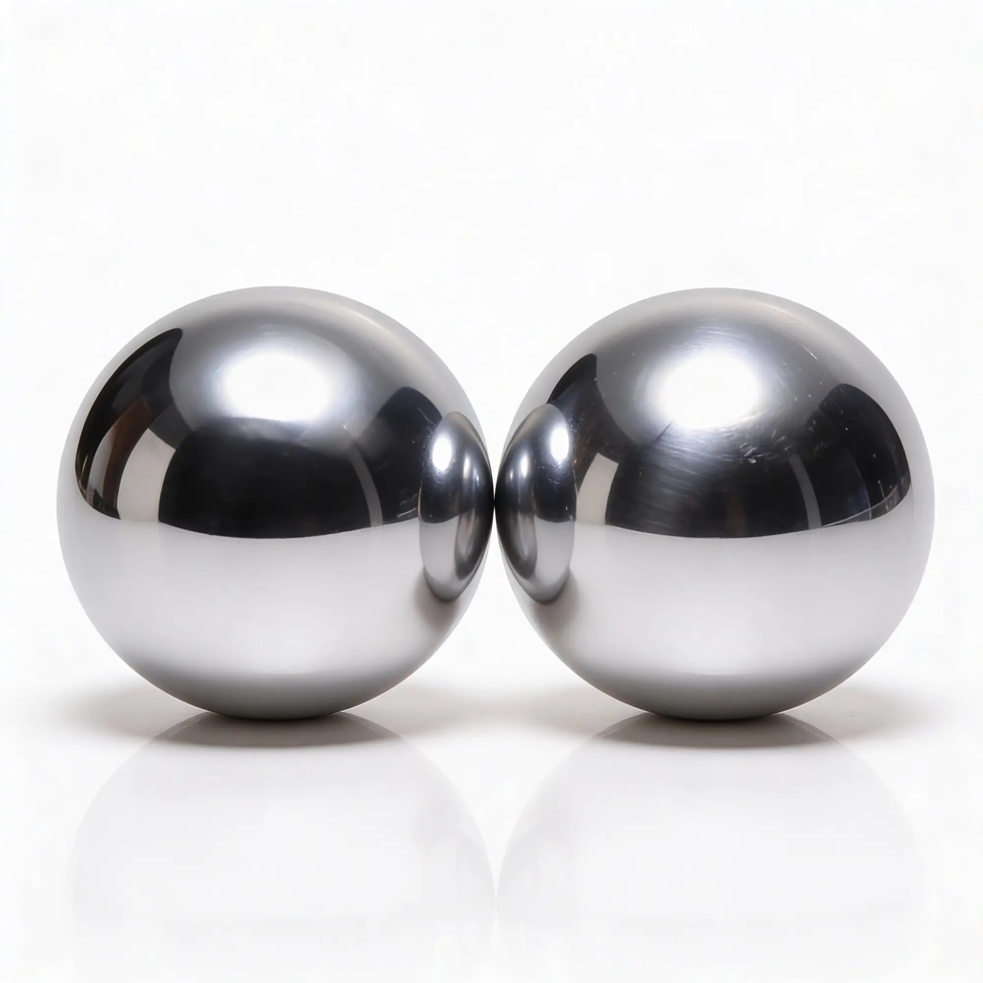 Two Master Series Titanica Steel Balls rest side by side on a glossy white surface, displaying mirrored reflections and striking highlights.