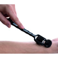 Hand using a black Master Series Transfix dual pinwheel sensory roller on a forearm against a white background.