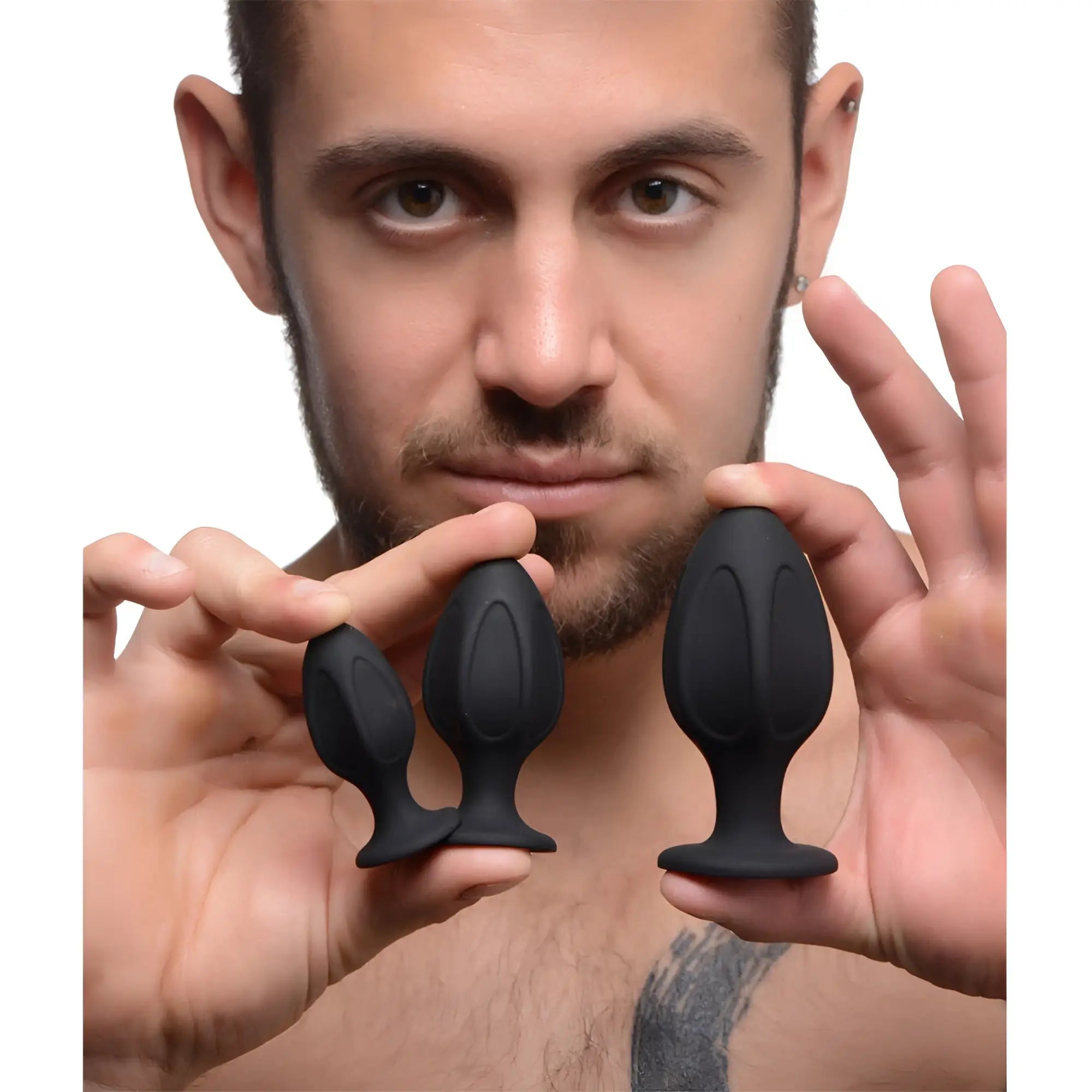 A man holds three smooth, matte black silicone Master Series Triple Juicers anal trainer plugs of increasing sizes.