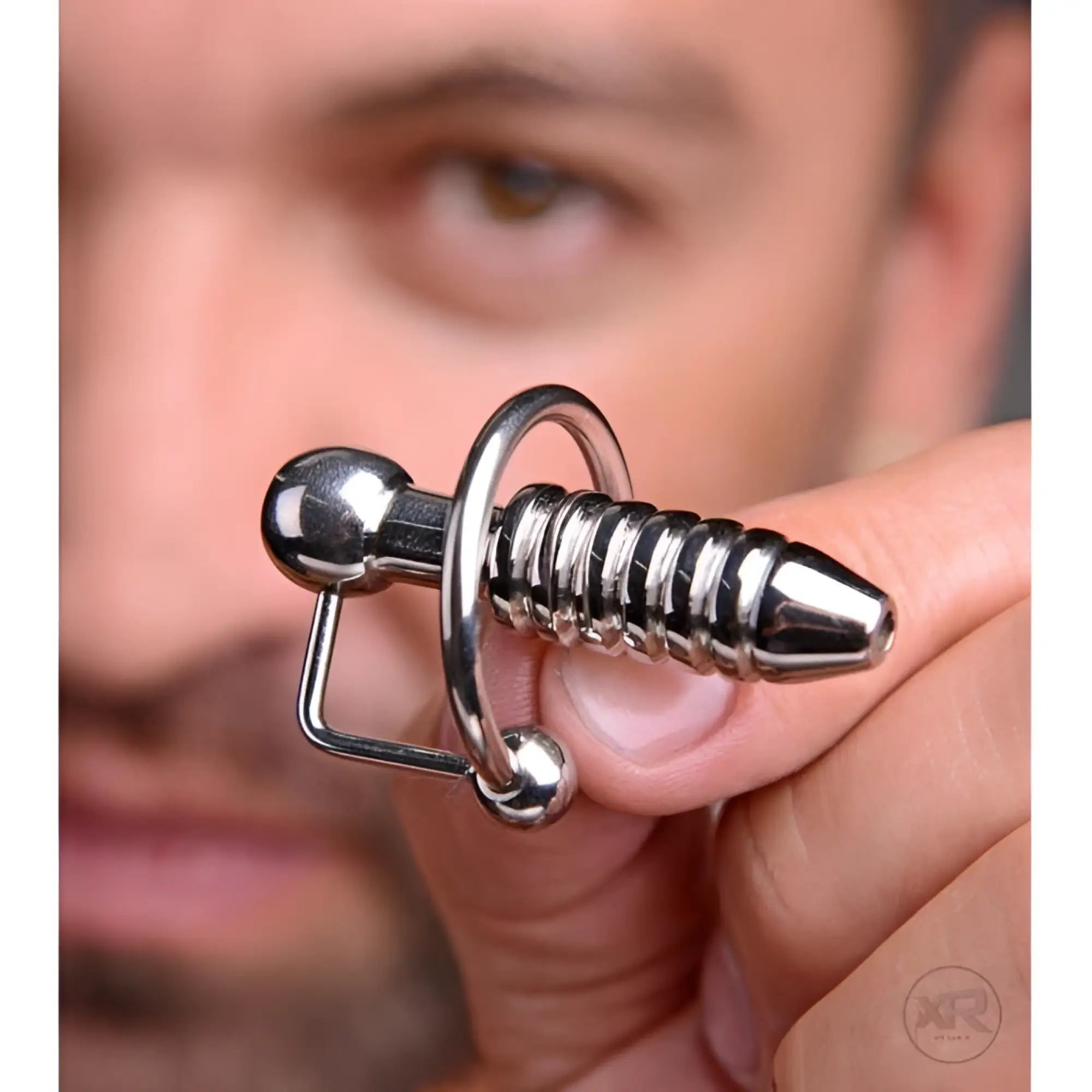 Silver Master Series XL ribbed urethral penis plug with a hollow core and a ball-bearing design held in fingers.
